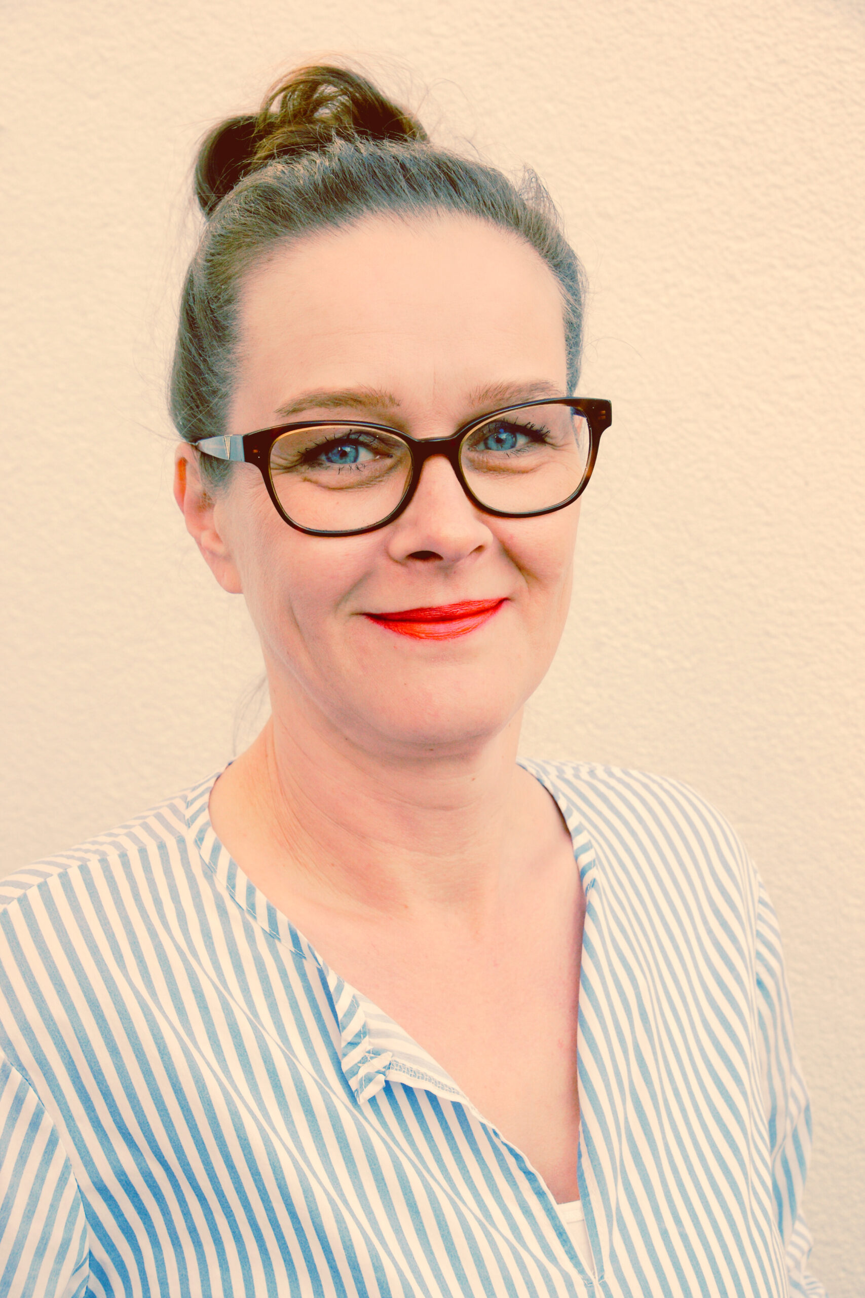 Auf dem Bild sieht man Jeannette Klemm im Profil. Sie trägt eine dunkle dick umrandete Brille. Ihre brünetten Haare trägt sie streng nach hinten zum Zopf gebunden. Der Hintergrund ist dezent rosa. 